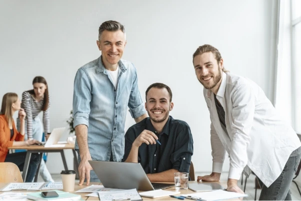 A group of men smiling at a laptop.